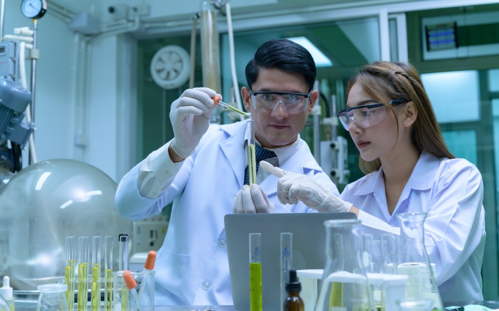 Older scientist in protective glasses and white coat setting up equipment for product extraction in GMP booth